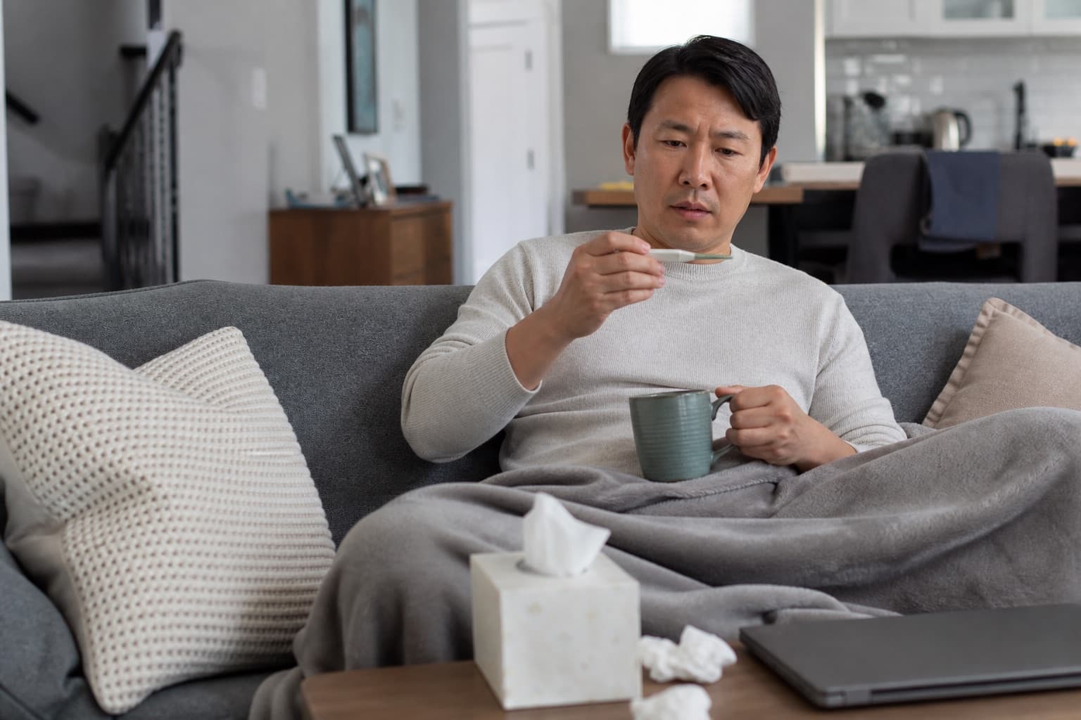A man checking his temperature while resting at home with cold or flu symptoms