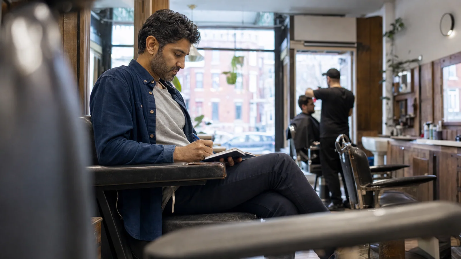 Un homme d’âge moyen note quelques exemples personnels en attendant dans un salon de barbier de quartier à Montréal avant un rendez-vous.